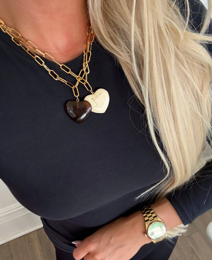 Person wearing a gold chain necklace with heart-shaped pendants and a gold watch.