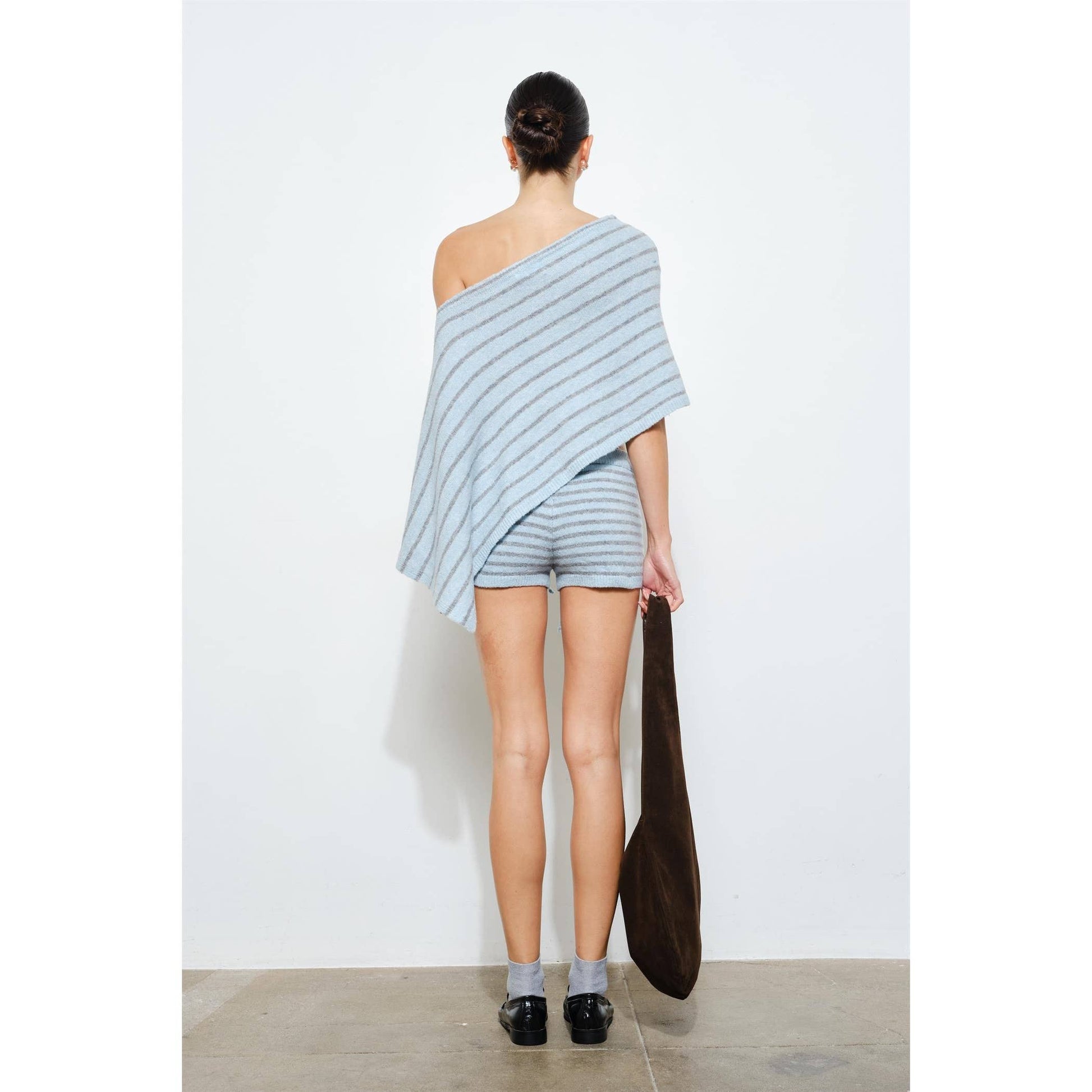 Person wearing a light blue striped outfit holding a brown bag against a white background