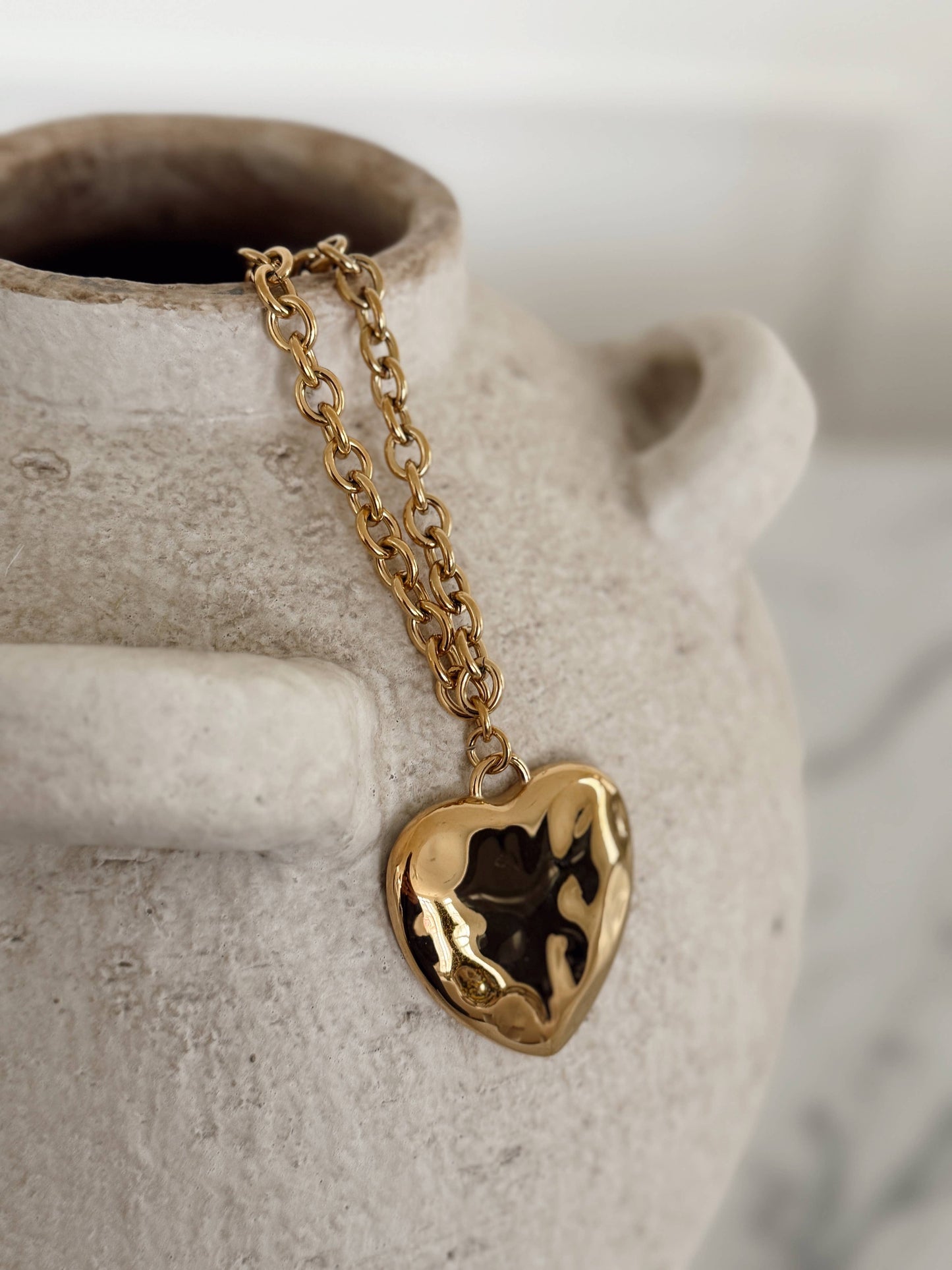 Gold heart-shaped pendant necklace on a ceramic vase