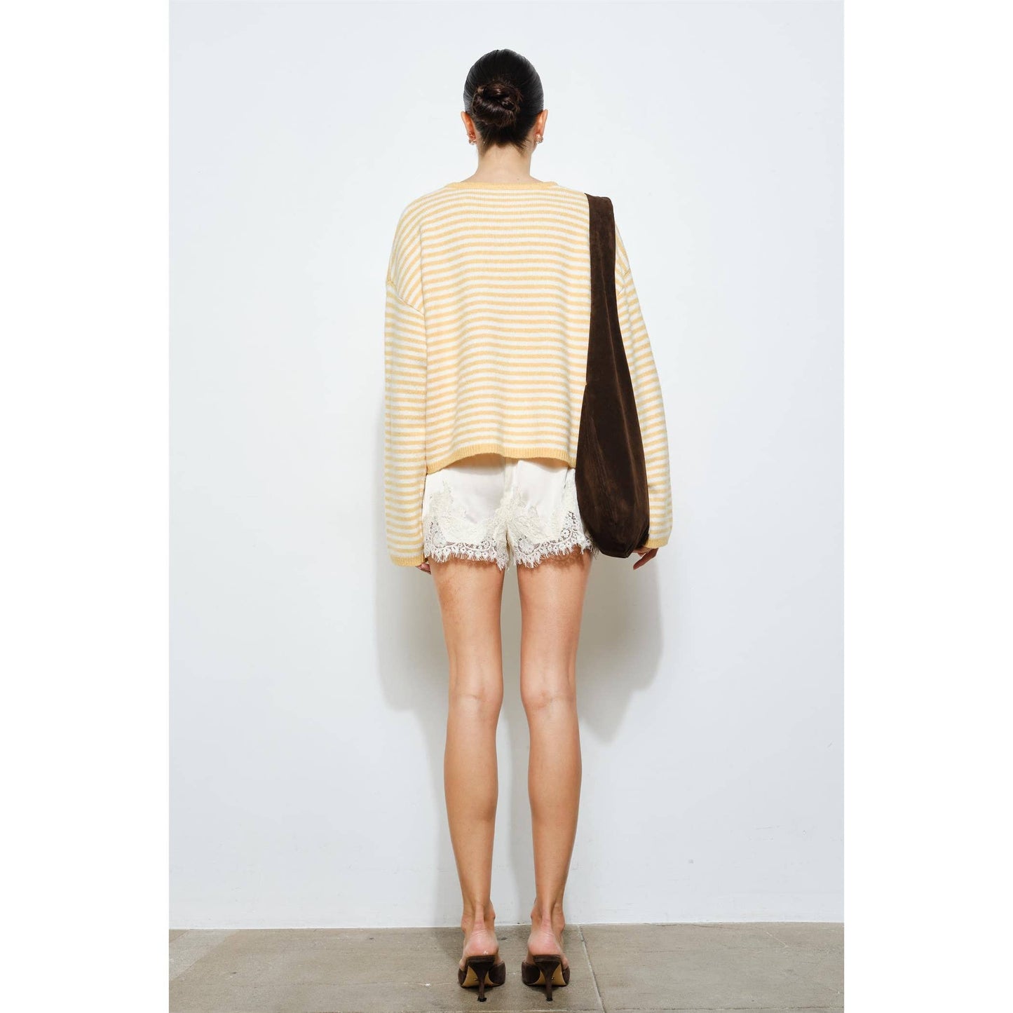 Person wearing a yellow striped sweater and white shorts, holding a brown bag against a white background