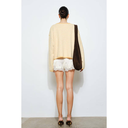 Person wearing a yellow striped sweater and white shorts, holding a brown bag against a white background